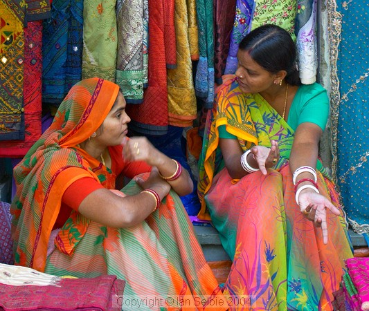 Two sales ladies chatting among their wares at the Janpath Lane textiles market, Delhi