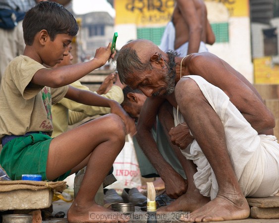 Shaving the heads of children and adults is a symbol of purification before bathing in the Ganges.   Here the children are shaving the elders